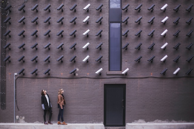 Two people standing beside a wall covered with surveillance cameras.